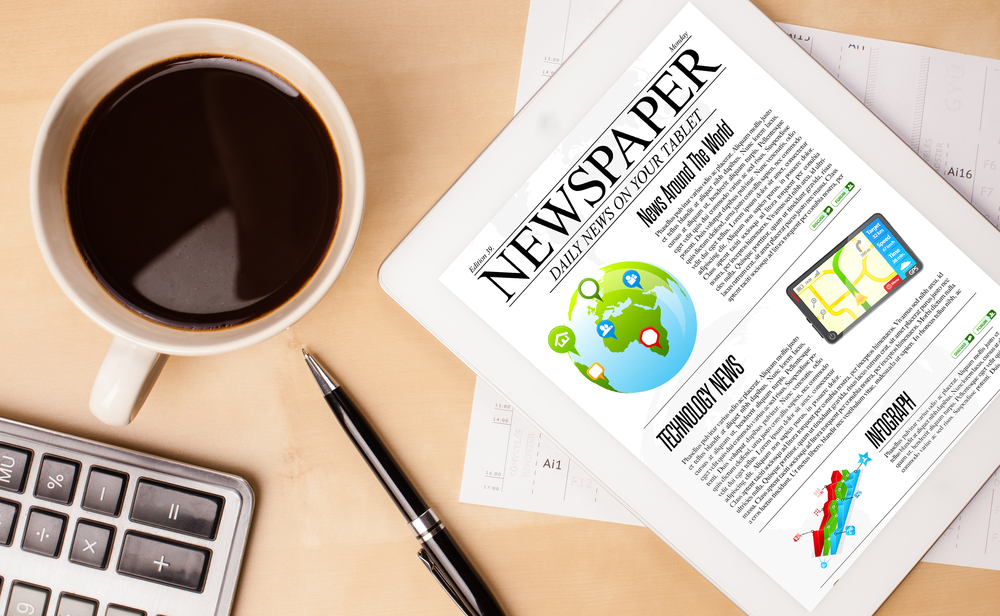 Workplace with tablet pc showing news and a cup of coffee on a wooden work table close-up